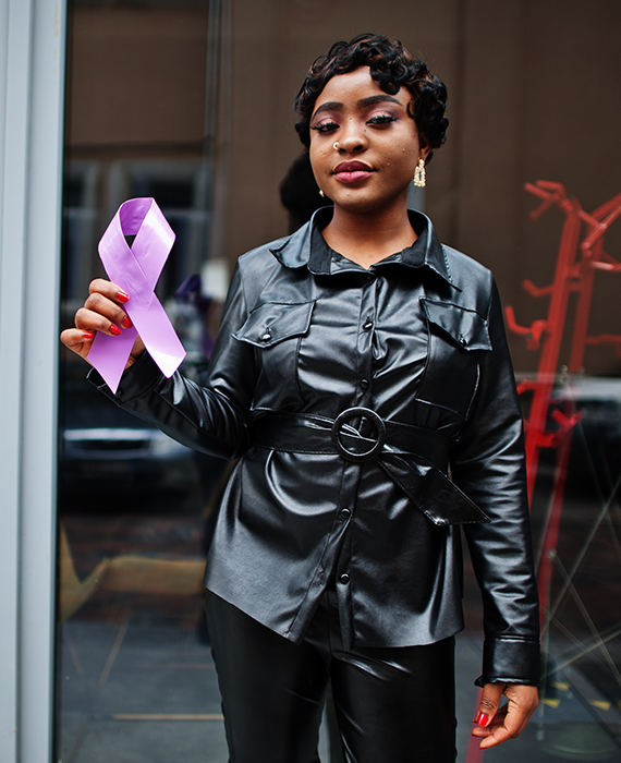 Young Black woman in front of a coffee shop, holding a purple awareness ribbon for lupus. 
