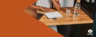Image of a person seated at a table, looking at a laptop