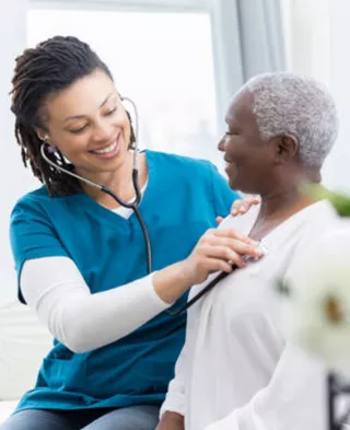Photo of a Black nurse checking an older Black woman's heart rate.