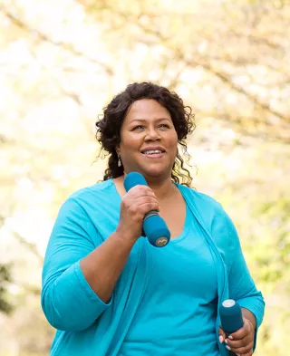 Image of a smiling woman walking outside with small dumbbells