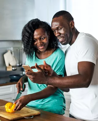 Couple chopping vegetables in their kitchen and referencing a recipe on their phone.