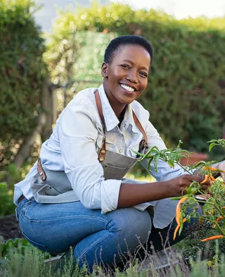 Photo of a smiling, healthy woman tending her vegetable garden