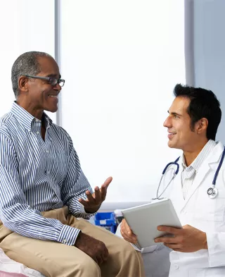 Photo of a smiling man on an examination table, speaking with his doctor.
