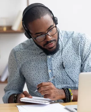 Photo of man taking notes while looking at his laptop.